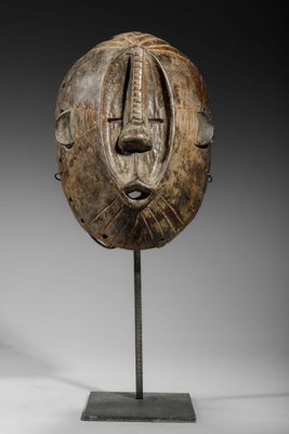 un masque en bois posé sur un socle métallique, sur fond blanc
