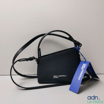 un sac à main noir orné d'une étiquette bleue, posé contre un mur blanc