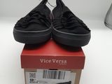 des Vans noires sans lacets posées sur une boîte rouge, sur une surface blanche