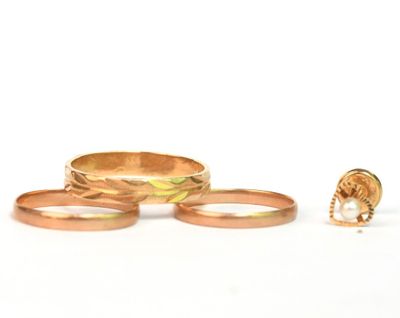 trois bagues en or et une bague ornée d'une perle sur fond blanc