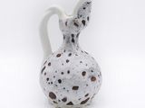 a white vase with brown spots on it on a white surface