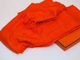 une écharpe orange et une boîte d'oranges posées sur une surface blanche