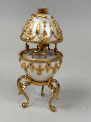 gold and white porcelain egg sitting on a stand on a white surface