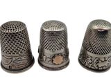 three silver thimbles are lined up on a white surface