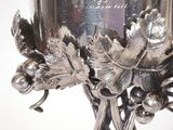 a silver vase that has a bunch of grapes on it