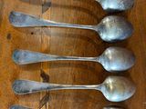 six silver spoons are lined up on a wooden table