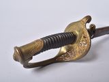 a gold colored sword with a black handle on a white surface
