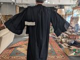 a man in a black robe and hat walking through a room