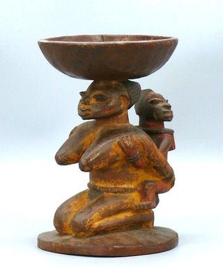 une sculpture en bois représentant une femme tenant un bol en équilibre sur la tête