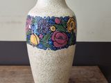 a white vase with flowers on it sitting on a wooden table