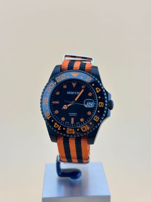 une montre orange et noire posée sur un socle, sur une surface blanche