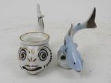 two ceramic fish and a cup on a white surface