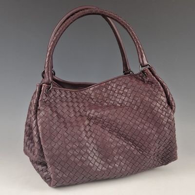 a purple woven leather handbag on a gray background