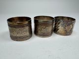 three silver cups with designs on them sitting on a white surface