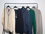 three men ' s sweaters hanging on a rack in a white room