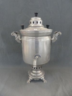 une théière ancienne plaquée argent, posée sur un support, sur un fond gris