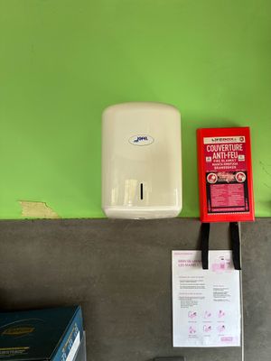 a green wall with a white paper towel dispenser and a red box on it