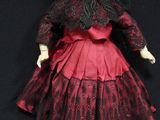 an old fashioned doll with a red dress and hat on a black background