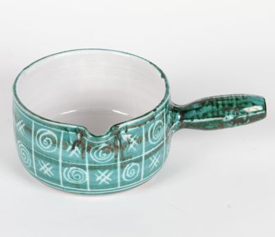 une petite tasse avec une anse posée sur une surface blanche