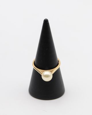 une bague en or ornée d'une perle posée au sommet d'un cône noir