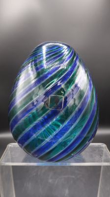 sphère en verre rayée de bleu et de vert, posée sur un socle en acrylique transparent