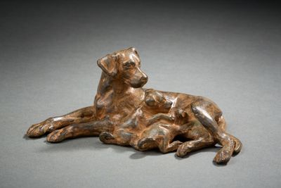 bronze sculpture of a dog laying down on a gray surface