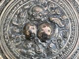 un plateau en argent orné d'un visage, posé sur une table