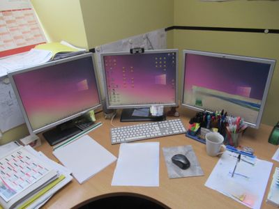 un bureau sur lequel se trouvent trois écrans d'ordinateur et un clavier