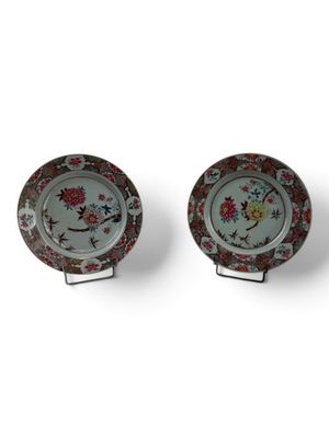 two plates with floral designs on them sitting on a stand