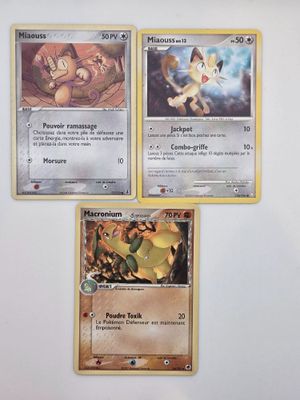 Trois cartes Pokémon sont posées sur une surface blanche, sur fond blanc.