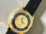 a gold watch on a black strap on a white surface
