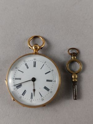 a small gold pocket watch and a key on a table