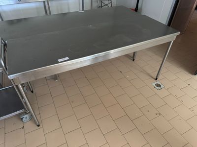 une table en acier inoxydable dans une cuisine, avec deux tabourets