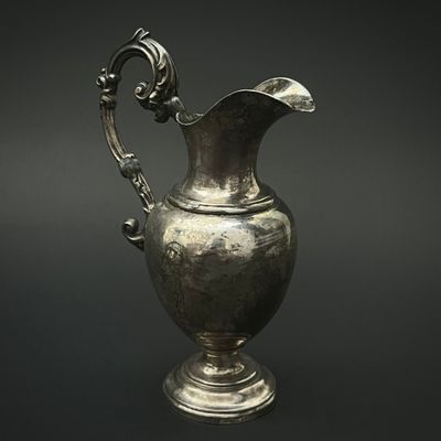 un pichet ancien en argent posé sur un socle, sur fond noir