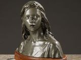 a bronze busturine of a woman with long hair on a marble surface