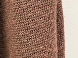 brown knitted sweater hanging on a hanger against a white wall