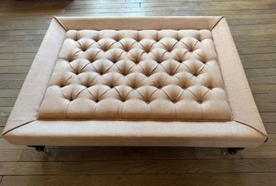 pouf rembourré beige monté sur roulettes, posé sur le parquet du salon