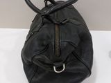 black leather handbag with zippers and handles on a white table