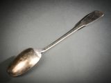 une cuillère en argent avec un manche de cuillère sur une surface grise