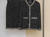 une veste et une jupe noires et blanches suspendues à un cintre devant un mur