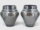 two silver vases sitting next to each other on a white surface