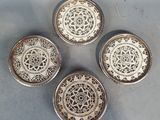 quatre sous-verres en argent ornés de motifs complexes, posés sur une table