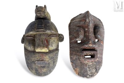 une paire de masques en bois représentant des visages, sur lesquels est perché un chat