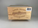 La boîte en bois contient une bouteille de vin posée sur une surface blanche.