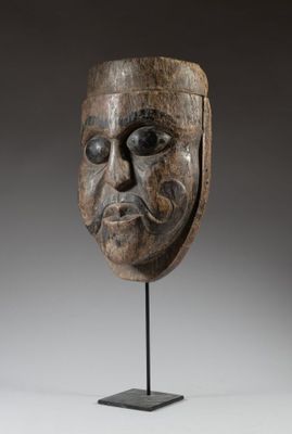 un masque en bois posé sur un socle, sur fond gris