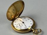 une montre de poche en or posée sur une surface blanche