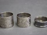 trois ronds de serviette en argent ornés de motifs, posés sur une table