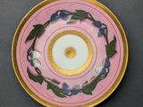 pink and gold plate with blue flowers and leaves on a black surface
