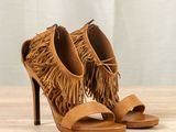 tan sued fringe sandals on a wooden table with a curtain in the background