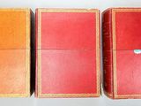 three red and orange books are lined up on a white surface